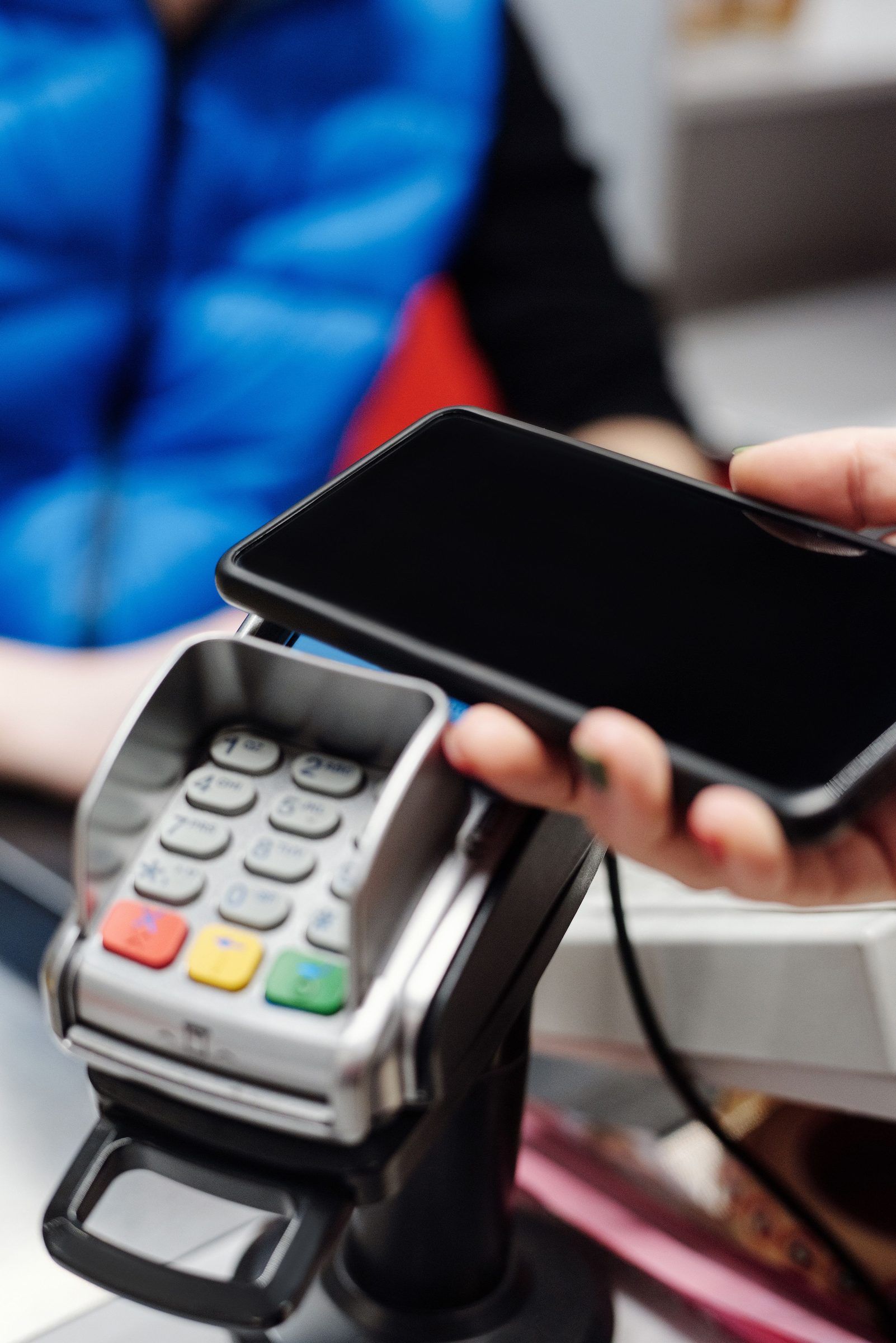 Una mano avvicina lo smartphone al terminale di pagamento in cassa.